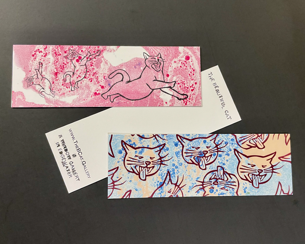 the Beautiful Cat bookmarks featuring leaping and hissing cats. The back of the bookmarks say, "The Beautiful Cat www.TheBCat.gallery a window gallery in Edgewater"