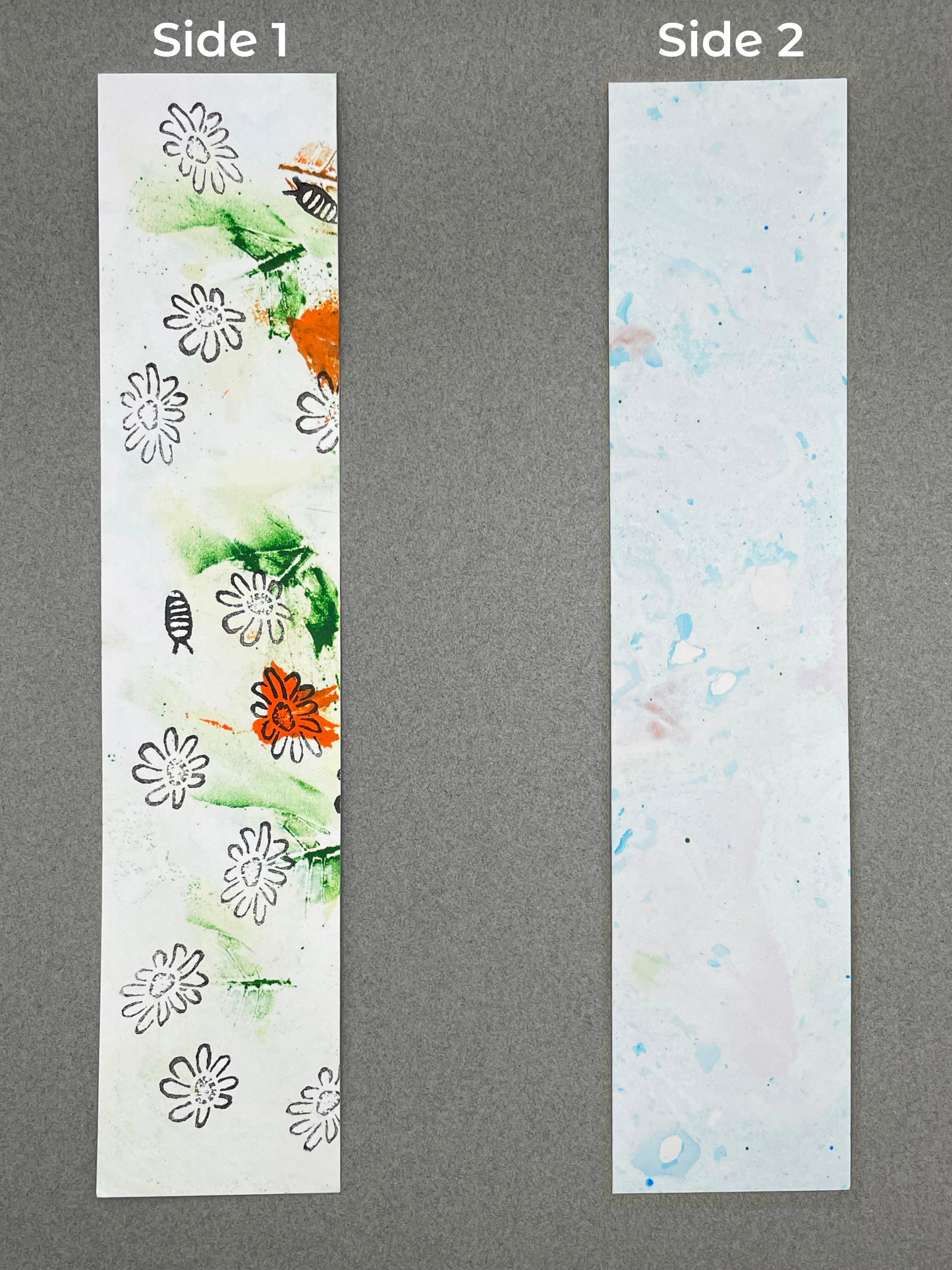 both sides of a bookmark are shown under their respective labels, which say "Side 1" and "Side 2". Side 1  shows smears of green and orange with chamomile flowers and a pill bug. Side 2 shows light blue marbling