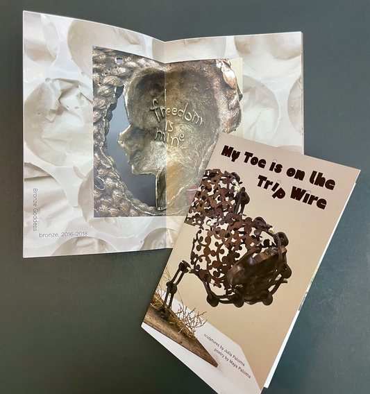 "My Toe is on the Trip Wire" exhibition catalog. A closed catalog is laying on an open one. The cover has a metal bison made of abstract Curley cues. The open spread has a hollow metal bust surrounded by metal hair and the inside of the bust says, "freedom is mine".