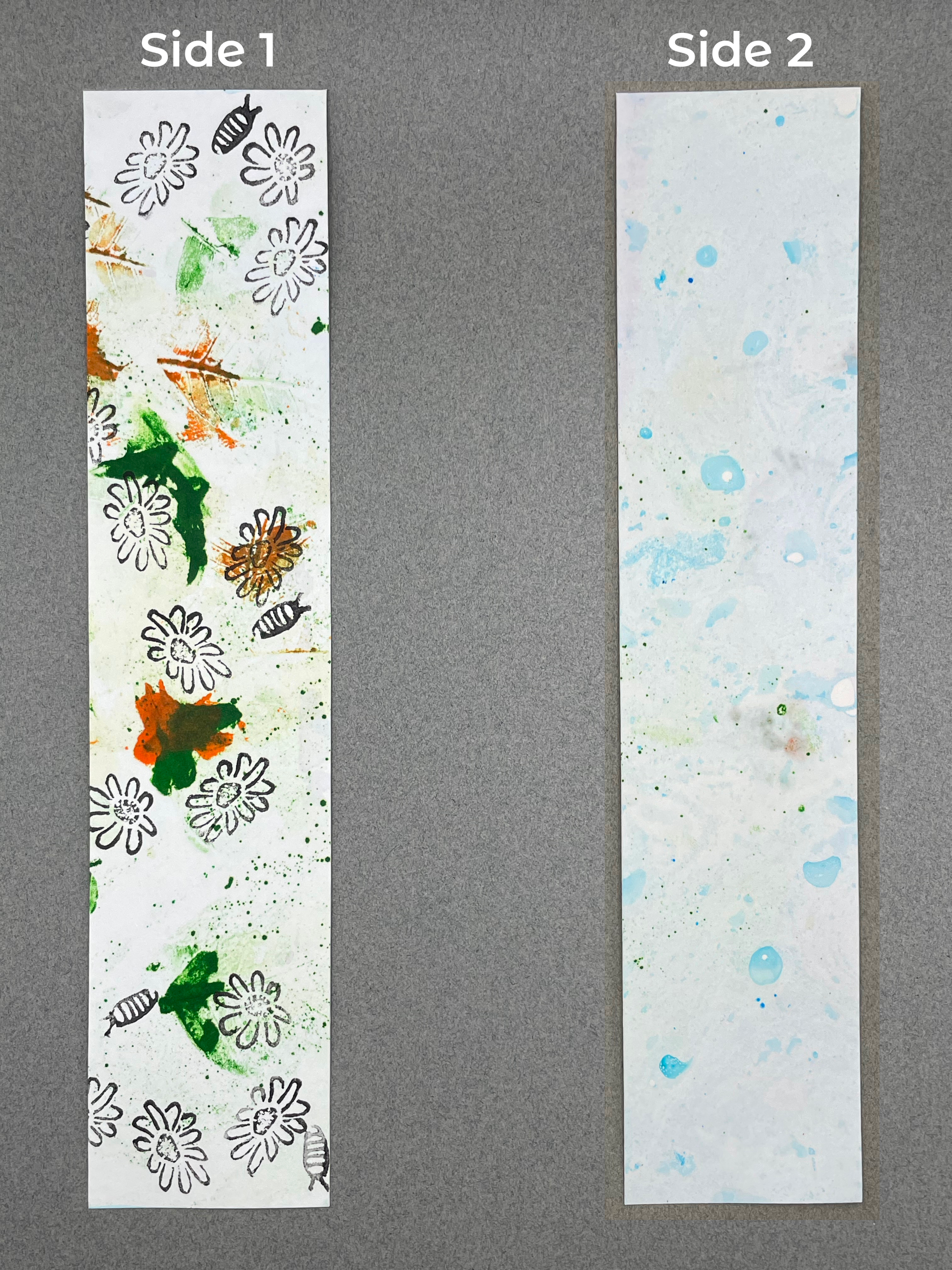 both sides of a bookmark are shown under their respective labels, which say "Side 1" and "Side 2". Side 1  shows smears of green and orange with chamomile flowers and a pill bug. Side 2 shows light blue marbling