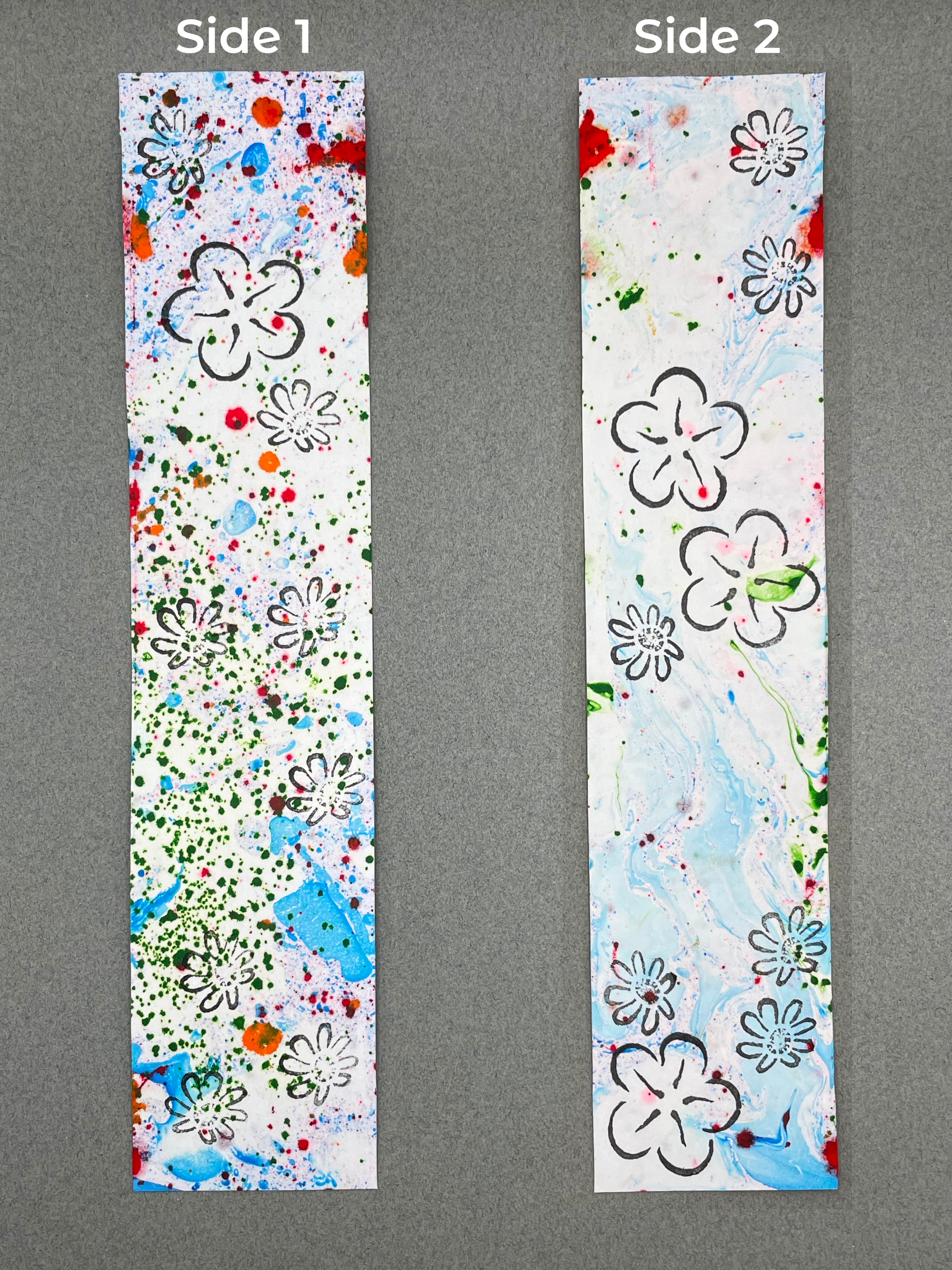 both sides of a bookmark are shown under their respective labels, which say "Side 1" and "Side 2". Side 1  shows dots of various sizes of blue, red, and green with chamomile flowers and a plum flower. Side 2 shows swirling blue marbling with splotches of red and green and has plum and chamomile flowers